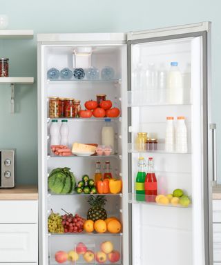 An image of an open fridge stacked high with colorful fruit and vegetables and bottles of milk, water, and juices