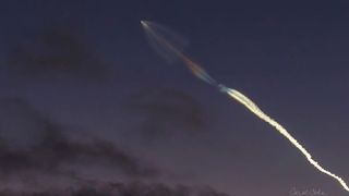 a trail of smoke wisps far away in the sky, tracing upward to a rocket. it is nighttime 