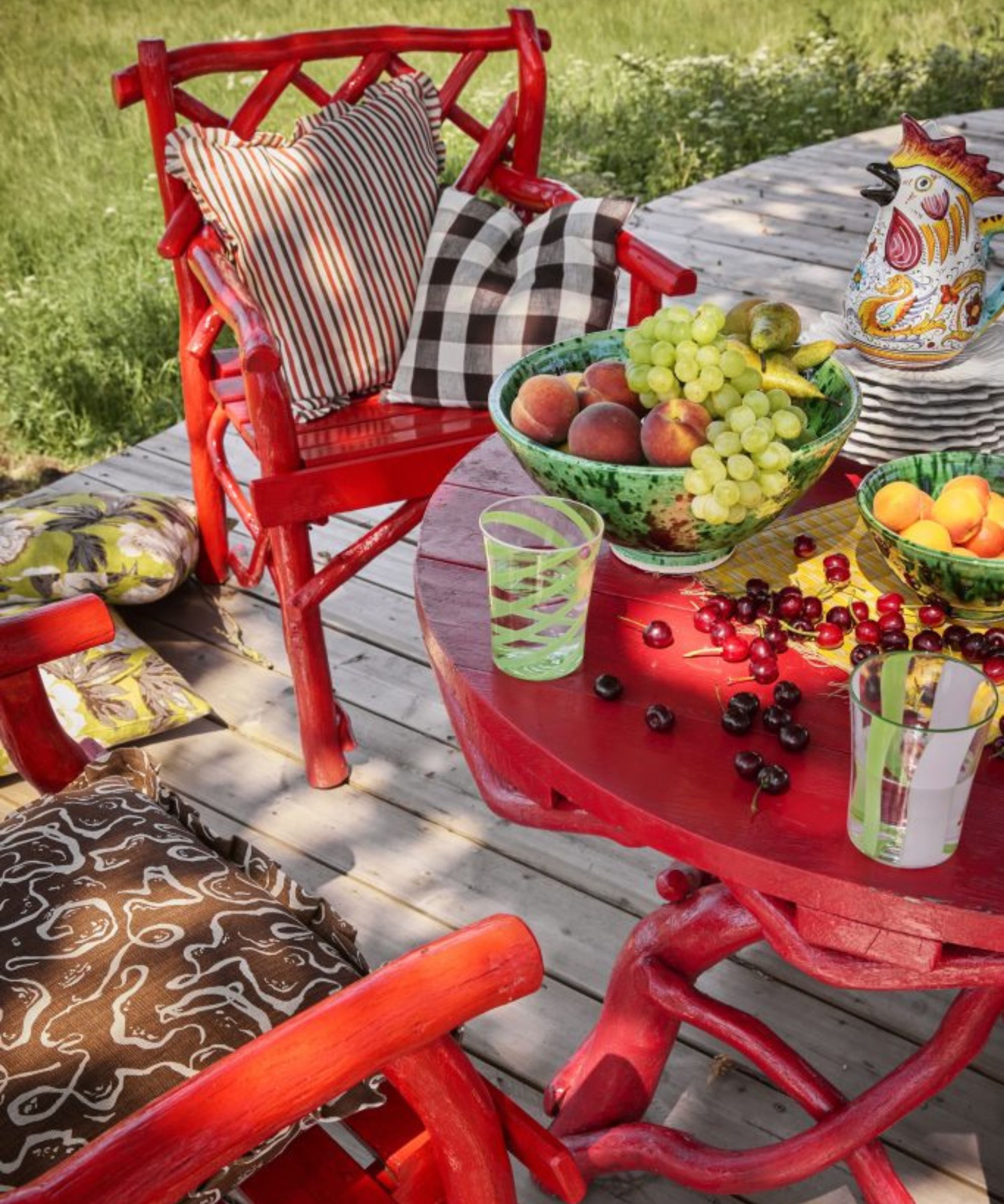 red wooden bistro table with cushions and a table filled with unique crockery, a big green bowl with fruit, and piles of cherries