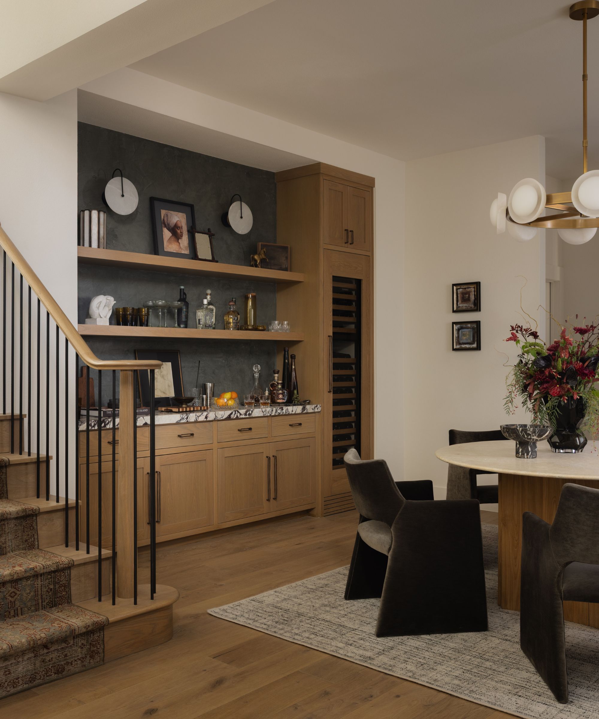 a neutral entryway with a modern wooden staircase with vintage runner rug. to the right is dining room with a home bar made from oak