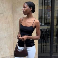 Influencer stands outside in Paris wearing a black spaghetti strap tank top with white capri pants and open-toe black patent heeled mules.