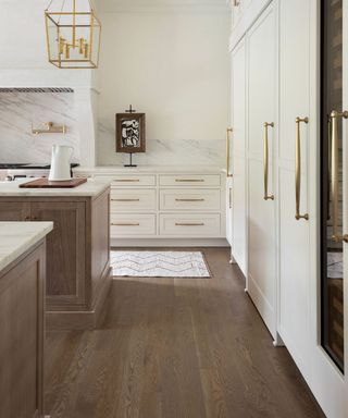 Kitchen with white cabinets with gold hardware, wood floor and wood island