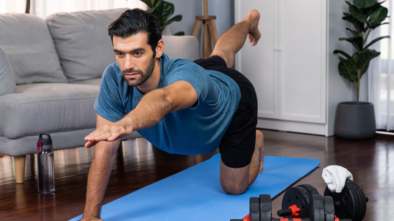 A man performing the core exercise &#039;bird dog&#039; in his living room