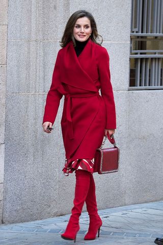 Queen Letizia wearing a red wrap around coat and tall boots
