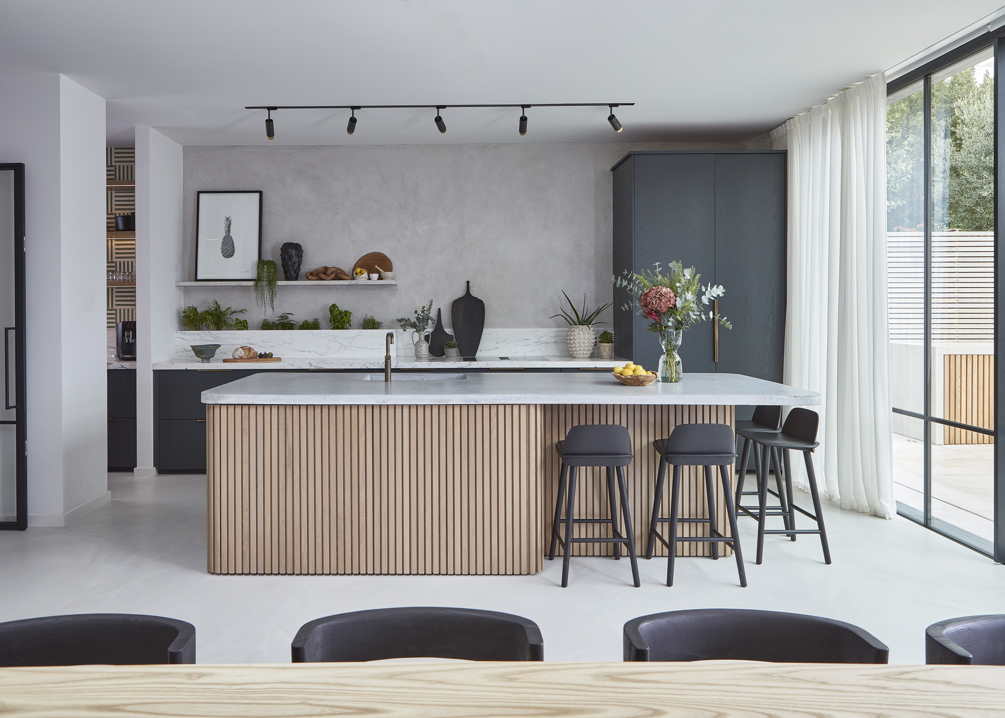 A modern kitchen with a fluted kitchen island, grey limewash walls, and dark grey cabinetry
