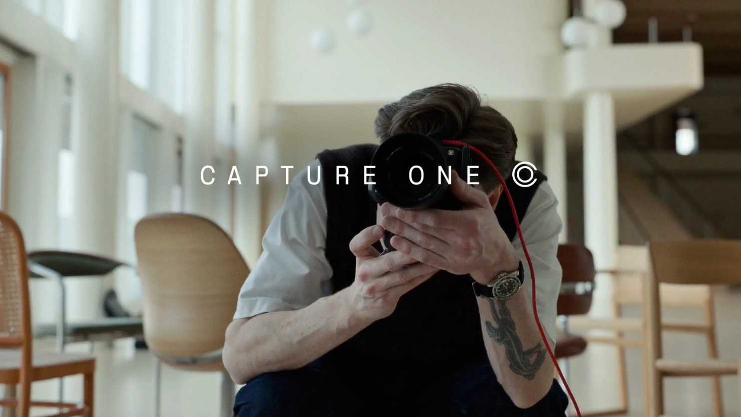 Image of photographer shooting towards viewer, with tethering cable coming out of camera and Capture One logo in centre of image