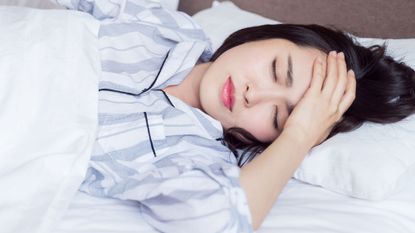 Woman in bed frowning, holding her head and suffering from sleep problems