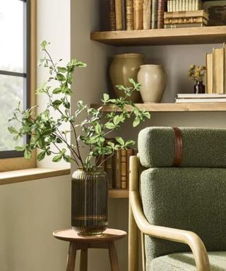 A neutral living room with a green armchair and green vase with faux plants