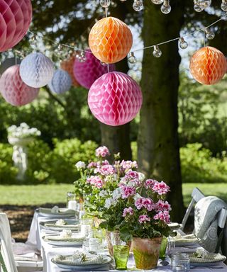 Garden table ideas with table laid with pot plants and paper pompoms overhead