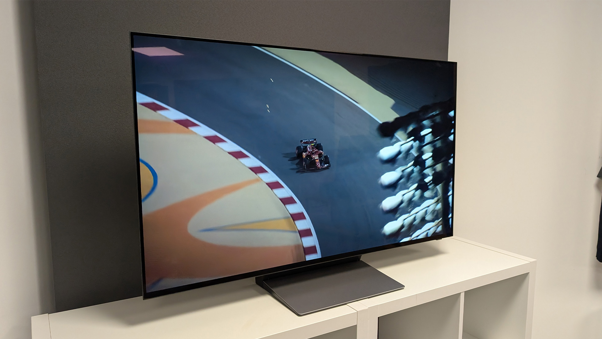Samsung S90F 48-inch OLED TV on white wooden furniture, on screen is aerial shot of F1 car on race track