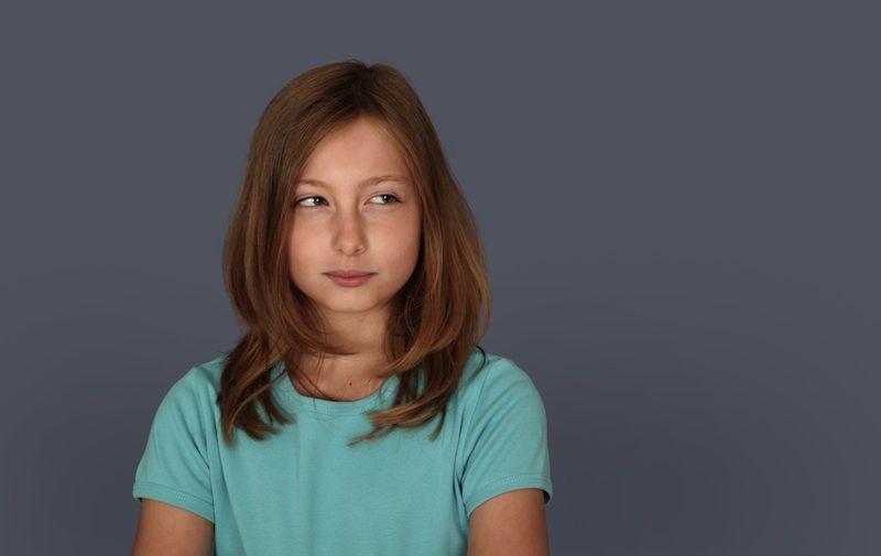 A young girl with a doubtful look in a blue shirt.