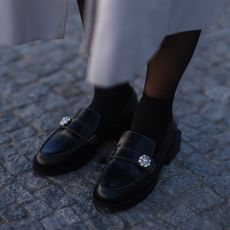 Aline Kaplan is seen wearing Chloe Faye brown leather bag, Palones beige trenchcoat, The Frankie Shop Black top, & other stories black mini skirt, Ganni black loafers and Carolina Lemke shades on March 18, 2022 in Berlin, Germany
