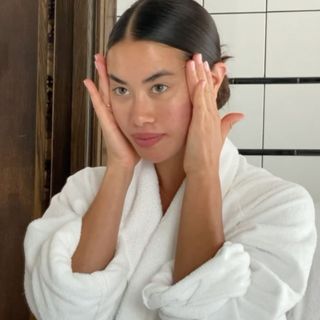 Woman in white dressing gown cleansing her skin in the mirror