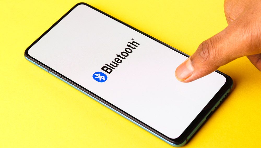 A thumb taps a generic smartphone with the Bluetooth logo and the word &#039;Bluetooth&#039; displayed on the screen.