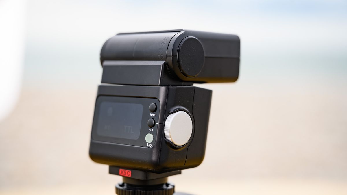 Closeup of the Godox iT32 camera flash and its rear display, the ocean is behind it
