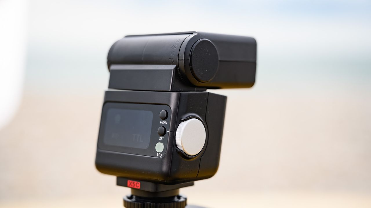 Closeup of the Godox iT32 camera flash and its rear display, the ocean is behind it