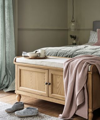 A storage bench with cabinet doors and a cushion top at the end of a bed