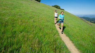 Two women running together down path on grassy hill