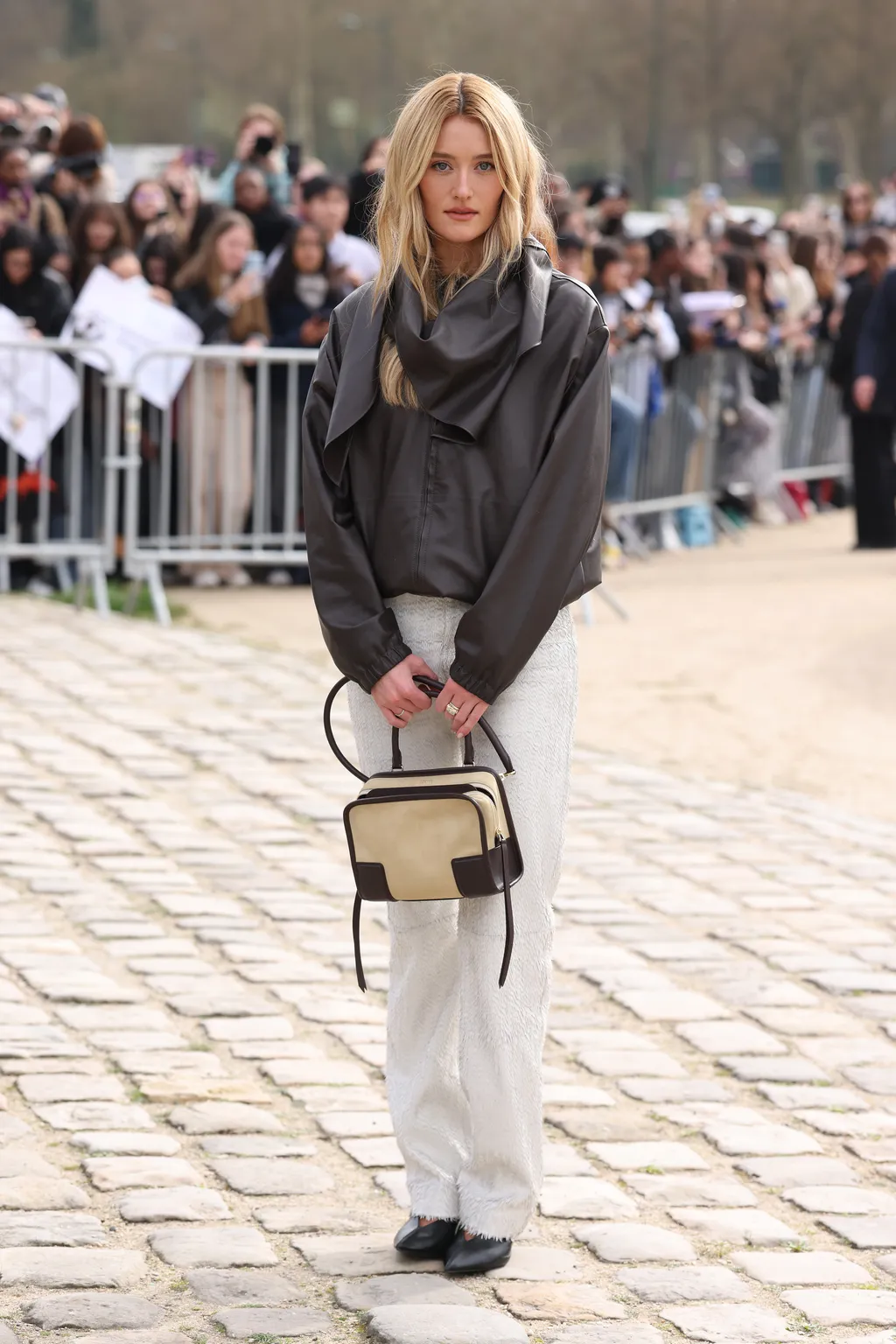 Sarah Pidgeon wears a gray jacket and white jeans with the beige Amazona 180 bag.