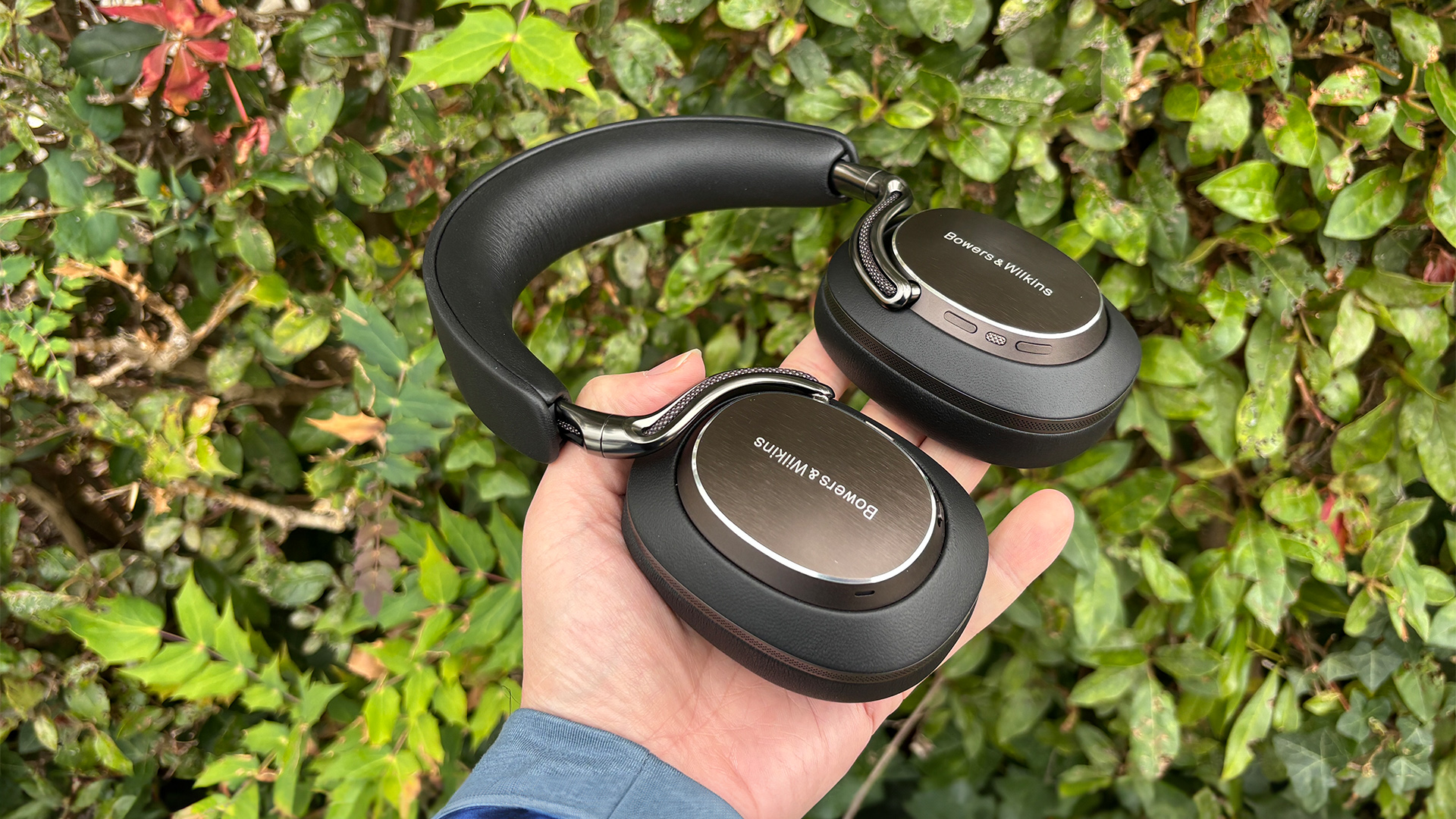 Bowers & Wilkins Px8 S2 wireless headphones held flat in hand in front of bush