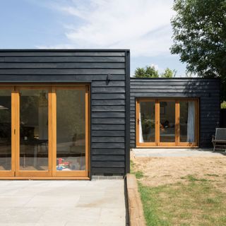 Black timber cladded bungalow with brown wooden stacker doors facing garden