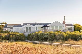 exterior of low grey painted beach house with coastal grasses and dunes with boardwalk to house