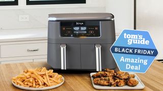 The Ninja Foodi two basket air fryer on a kitchen worktop with a plate of chicken and a plate of fries in front of it, demonstrating the dual zone cooking.