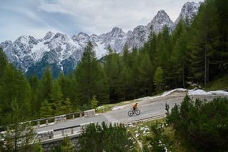 A road cyclist on a Slovenian climb with snow capped mountains in the background