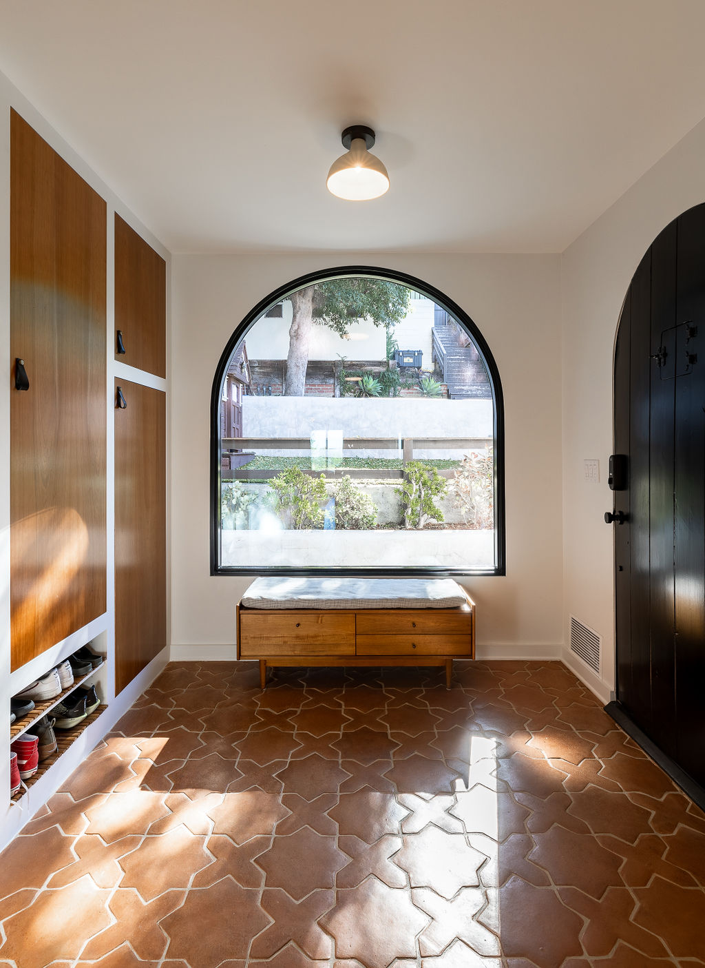 A modern entryway with built-in storage wall and an arched window.