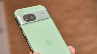 Google Pixel 8a i grønt holdes opp av en hånd.