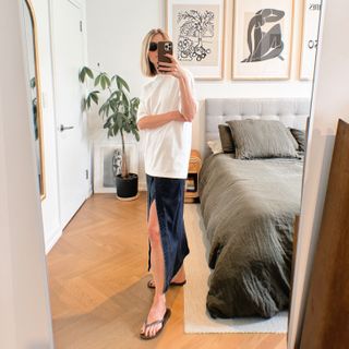 Natalie Cantell taking a mirror selfie in her NYC apartment wearing an oversized white Tibi t-shirt, denim Tibi skirt, Celine eyewear, and brown Havaiana flip-flops.