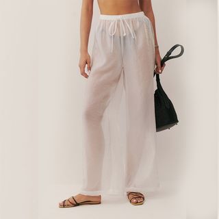 Reformation model wearing white sheer pants with black strappy sandals