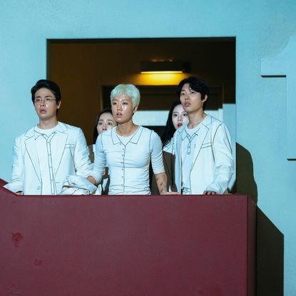 a group of people dressed in white (Park Jeong-min as Seventh Floor, Lee Zoo-young as Second Floor, Ryu Jun-yeol as Third Floor) stand on a balcony next to a number 1 sign, in 'The 8 Show'