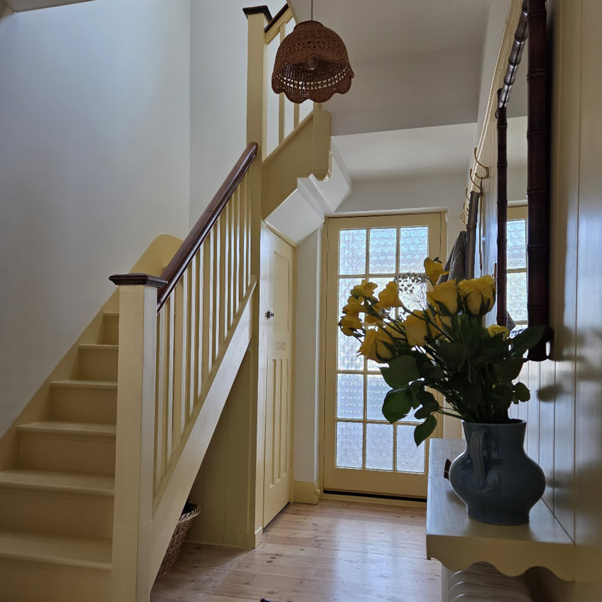 Hallway and stairs with woodwork painted yellow, including the stairs and a wicker lampshade on the ceiling light