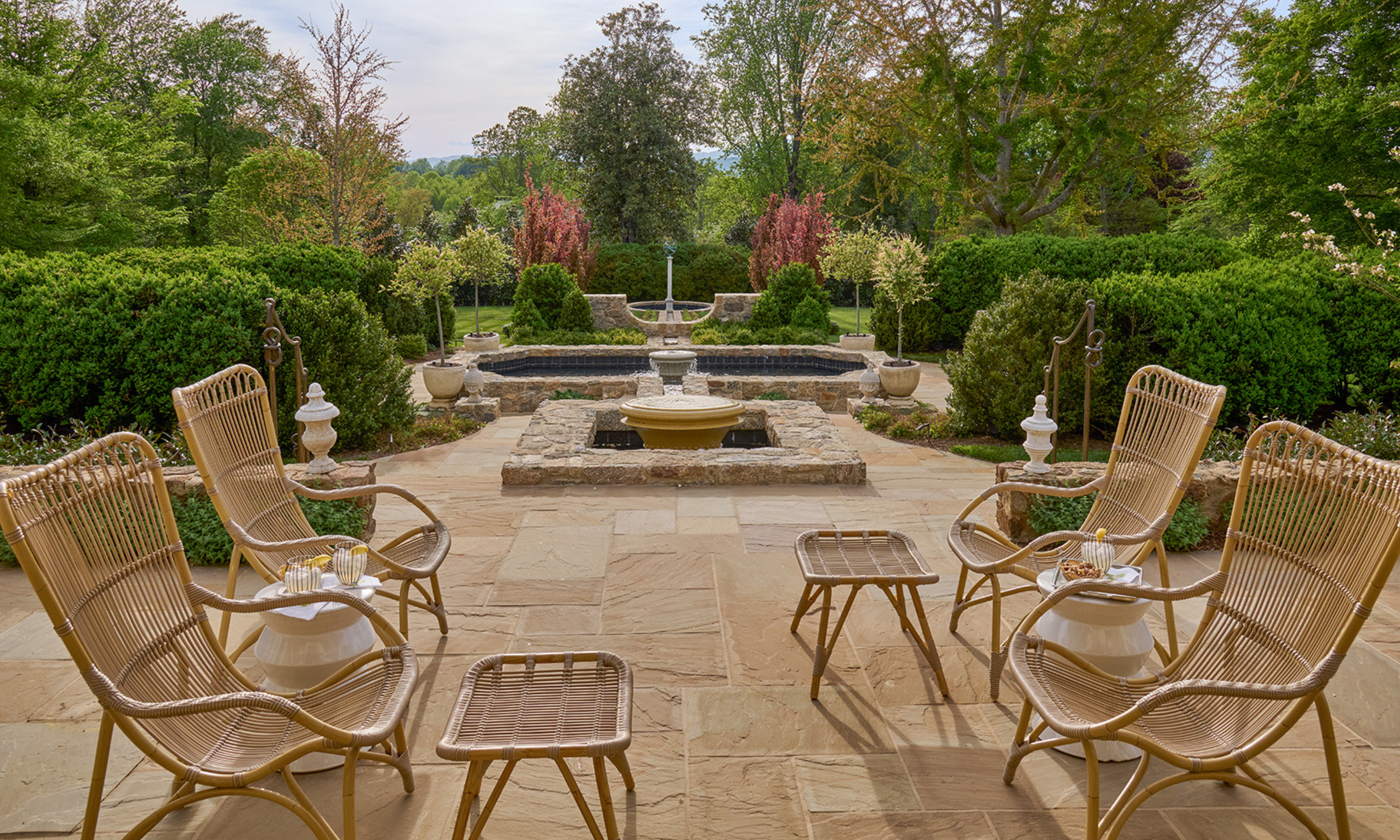 Large stone patio with wicker seating with mature planting and water feature in the background