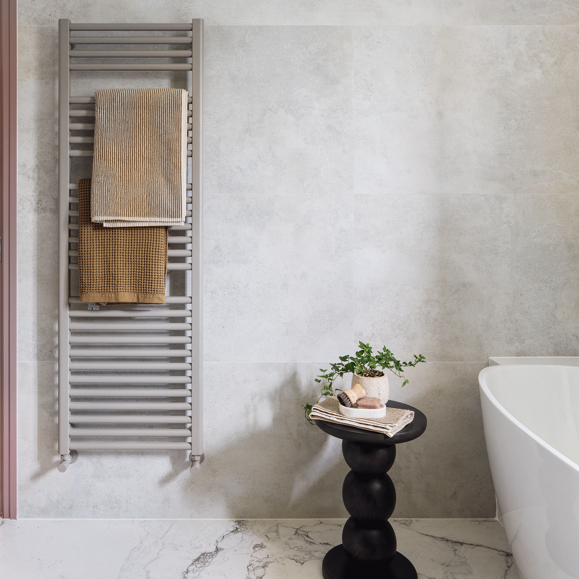 a grey/beige wall hung towel radiator beside a bath tun and a statement side table with marble walls