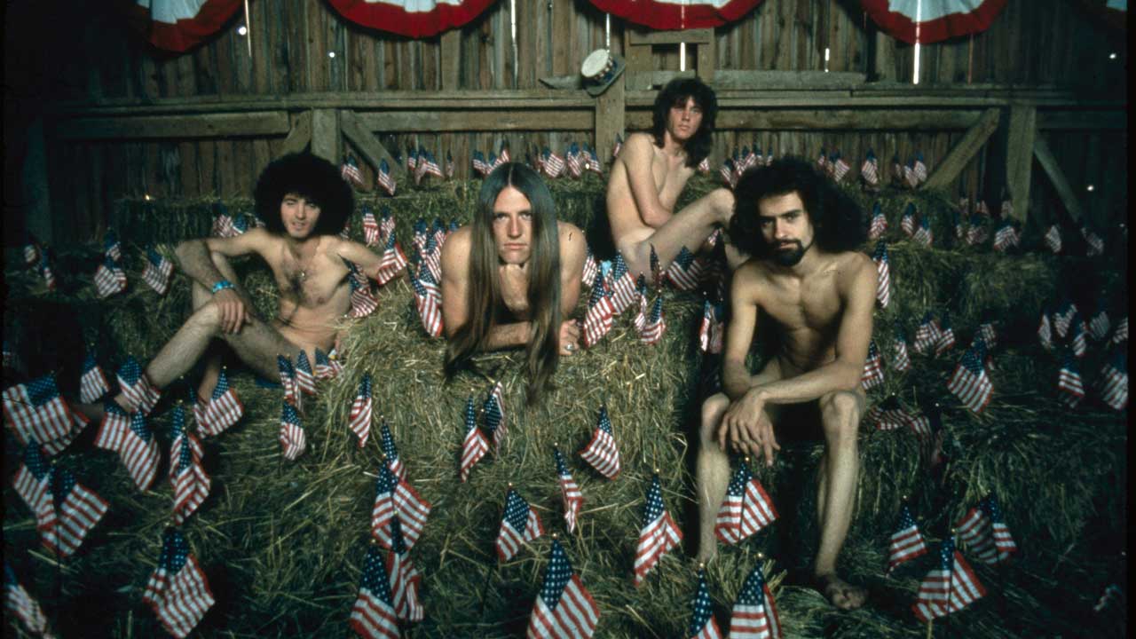 Grand Funk Railroad pictured on nude on a haystack in a barn surrounded by US flags