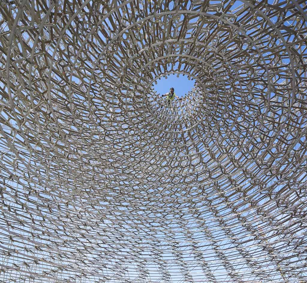 Interior view from below of the aluminium mesh ’beehive’ structure at the UK Pavilion - the structure has a hole at the top where a person can also be seen