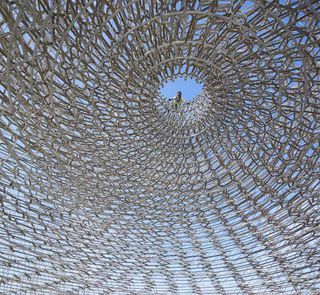 Interior view from below of the aluminium mesh ’beehive’ structure at the UK Pavilion - the structure has a hole at the top where a person can also be seen