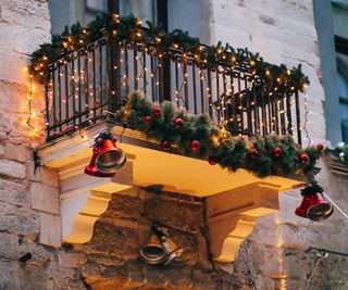 Stylish christmas decorations, red jingle bells, lights, fir branches with ornaments on balcony