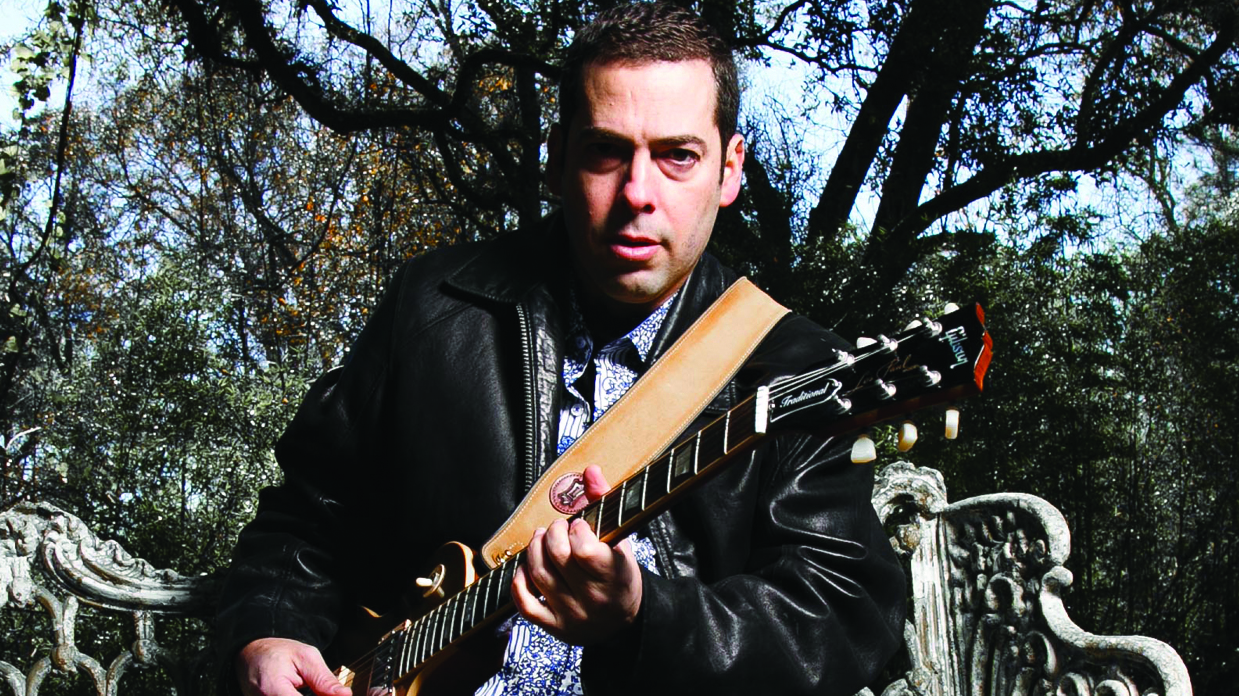 Albert Castiglia playing an electric guitar in a garden.