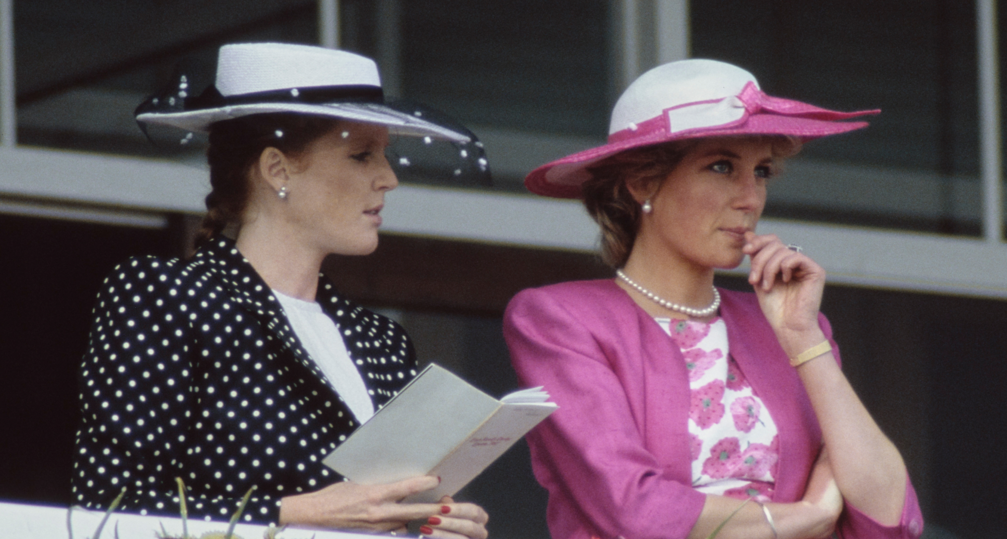 Sarah Ferguson wearing a polka dot suit standing next to Princess Diana in a pink jacket and white and pink hat