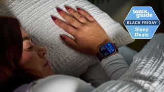 Our sleep tech reviewer in bed with white sheets wearing the Apple Watch Series 10 with purple strap displaying sleep stages screen on right wrist with Tom's Guide Black Friday sleep deals logo