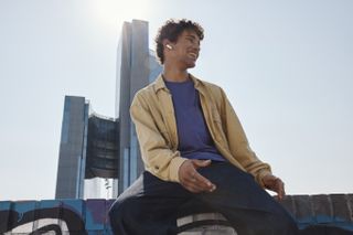 A person psoing next to a skyscraper while wearing the JBL Tune 230NC earbuds