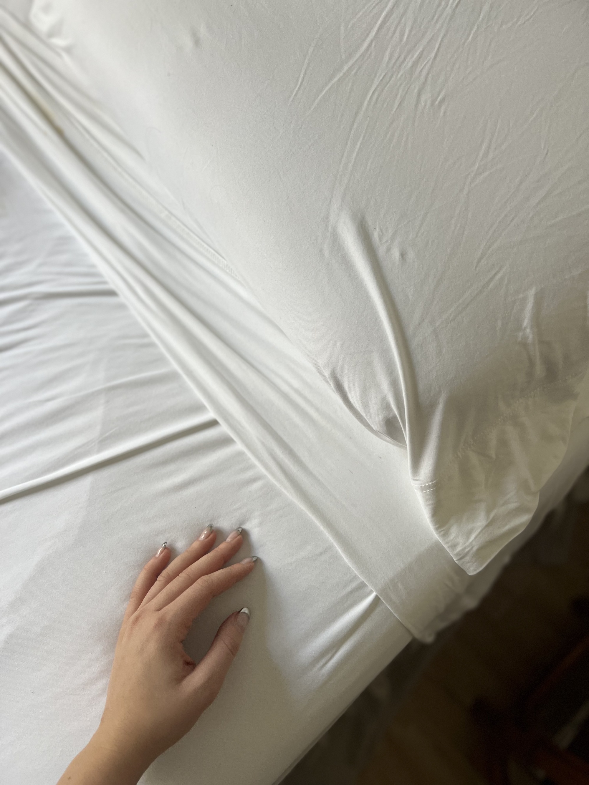 Image of a hand touch a set of white bedsheets on a bed