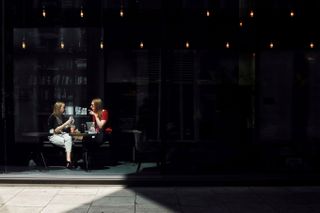 Candid photograph of two women drinking in a cafe's outdoor seating area. Photographed by Sean Tucker