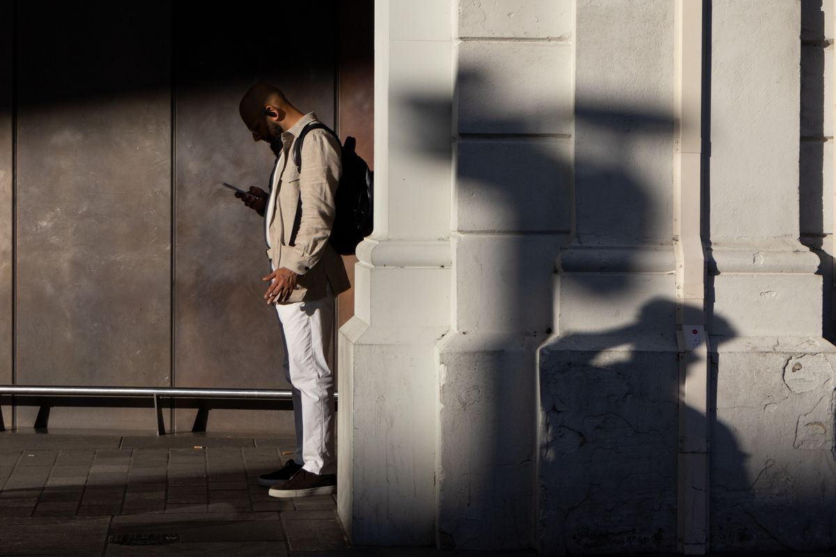 A man standing in the shade at a station reading his phone