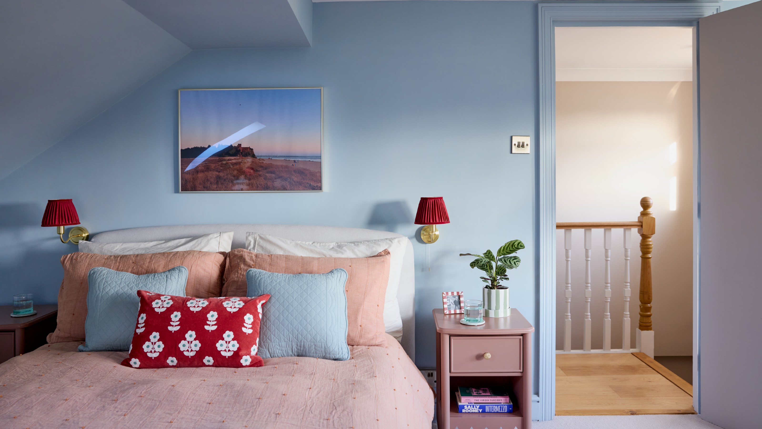 A bedroom painted in a sky blue shade with a slanted ciling and pink bed linen