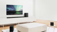 the LG SN11RG Dolby Atmos Soundbar beneath a TV showing an image of the northern lights, with the rear speakers and subwoofer