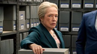 Kathy Bates stands amidst shelves with file boxes holding one grey box while staring at the camera on Matlock.
